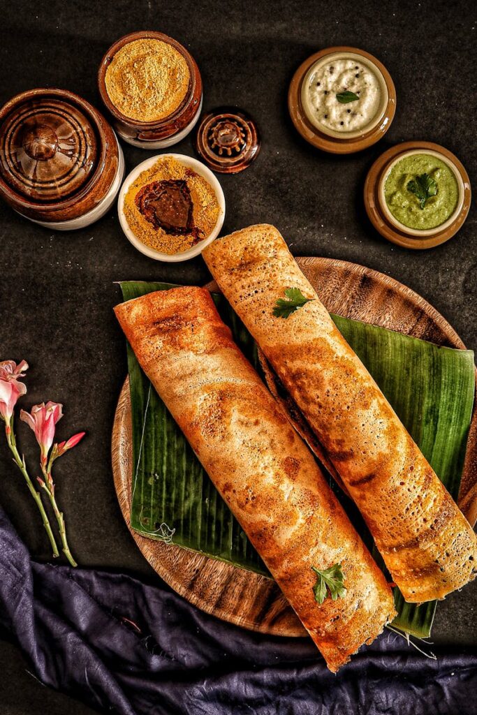 Delicious traditional dosa served with a variety of Indian chutneys and sambar on banana leaves.