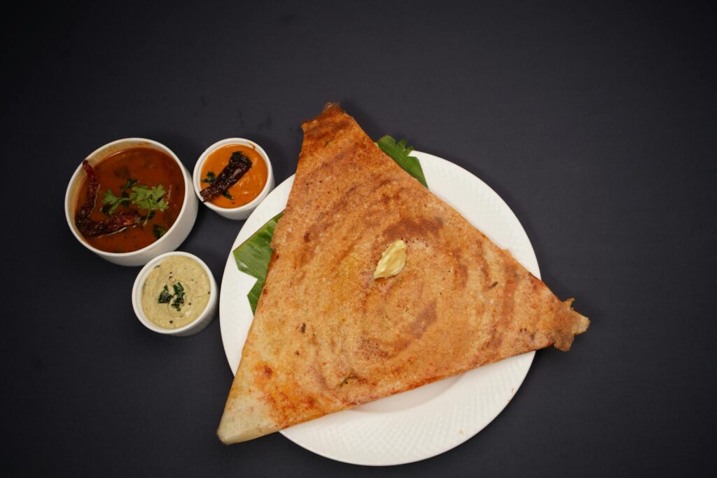 Crispy triangular dosa served with traditional chutneys and sambar on a black background.